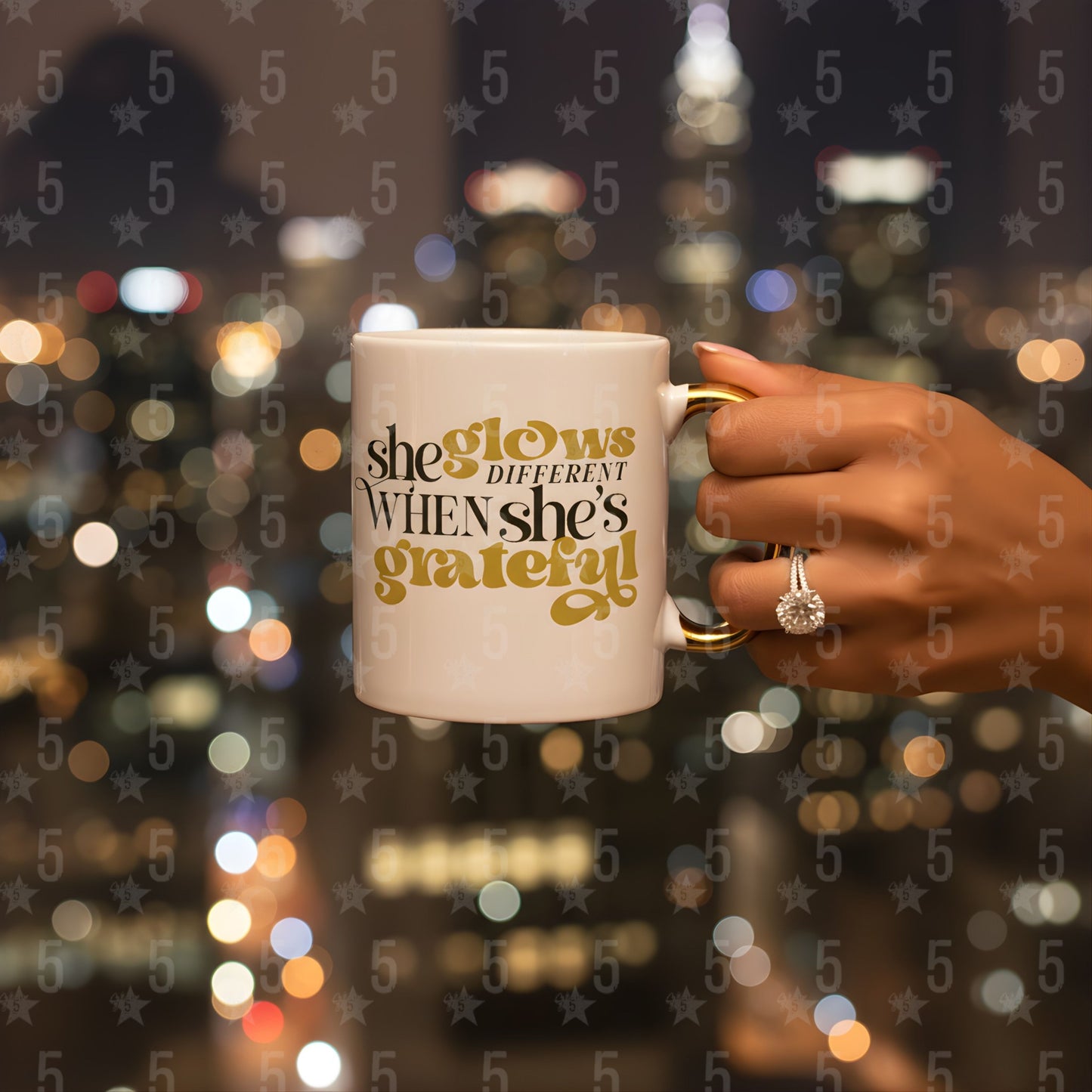Person holding a mug with 'she glows different when she's grateful' text against a blurred cityscape background.