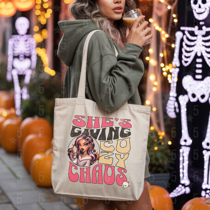 Person holding a tote bag with a graphic design and text, surrounded by Halloween decorations.