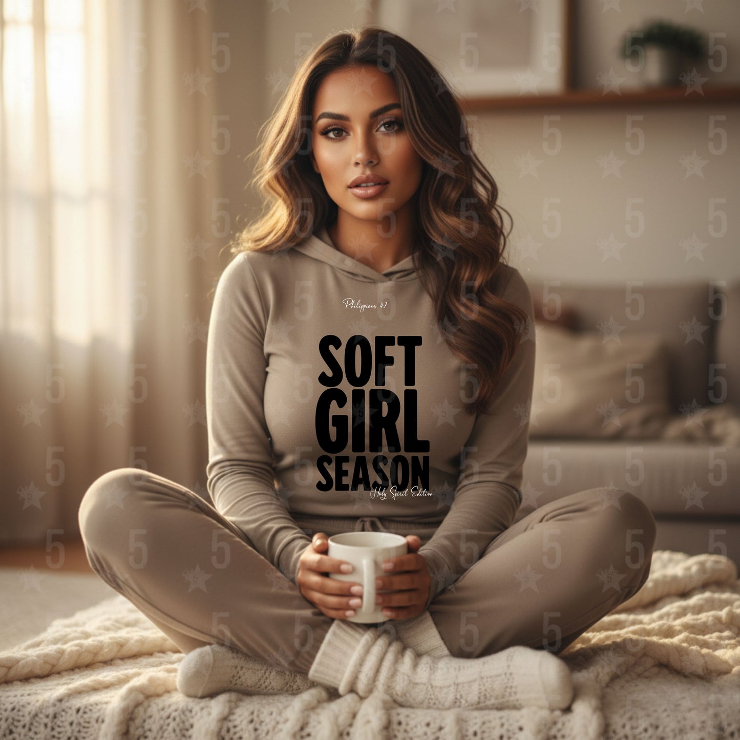 Woman wearing a hoodie with 'Soft Girl Season' text, sitting on a bed holding a mug.