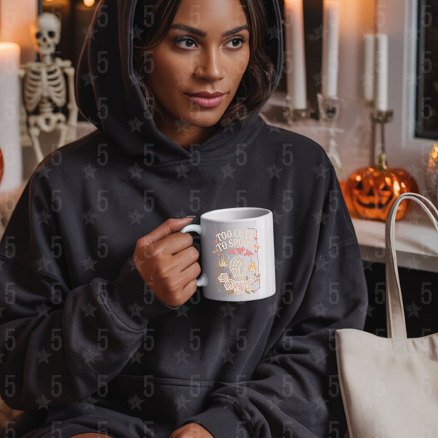 Woman in a black hoodie holding a mug with Halloween-themed design, sitting in a cozy room with Halloween decorations.