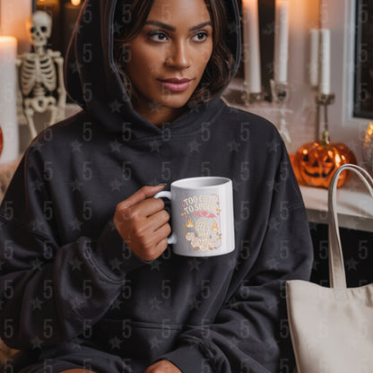 Woman in a black hoodie holding a mug with Halloween-themed design, sitting in a cozy room with Halloween decorations.