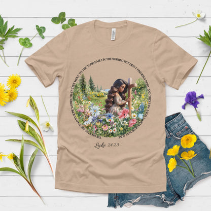 Beige t-shirt with a woman at a cross floral design, placed on a wooden surface with flowers around.