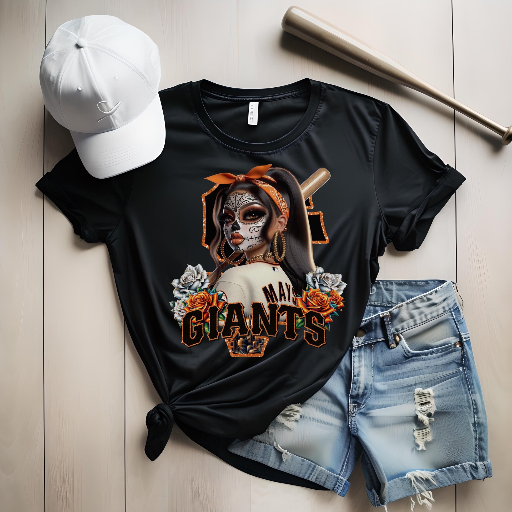 Black t-shirt with sf giants dia de los muertos design, white cap, and denim shorts on a light wooden surface.