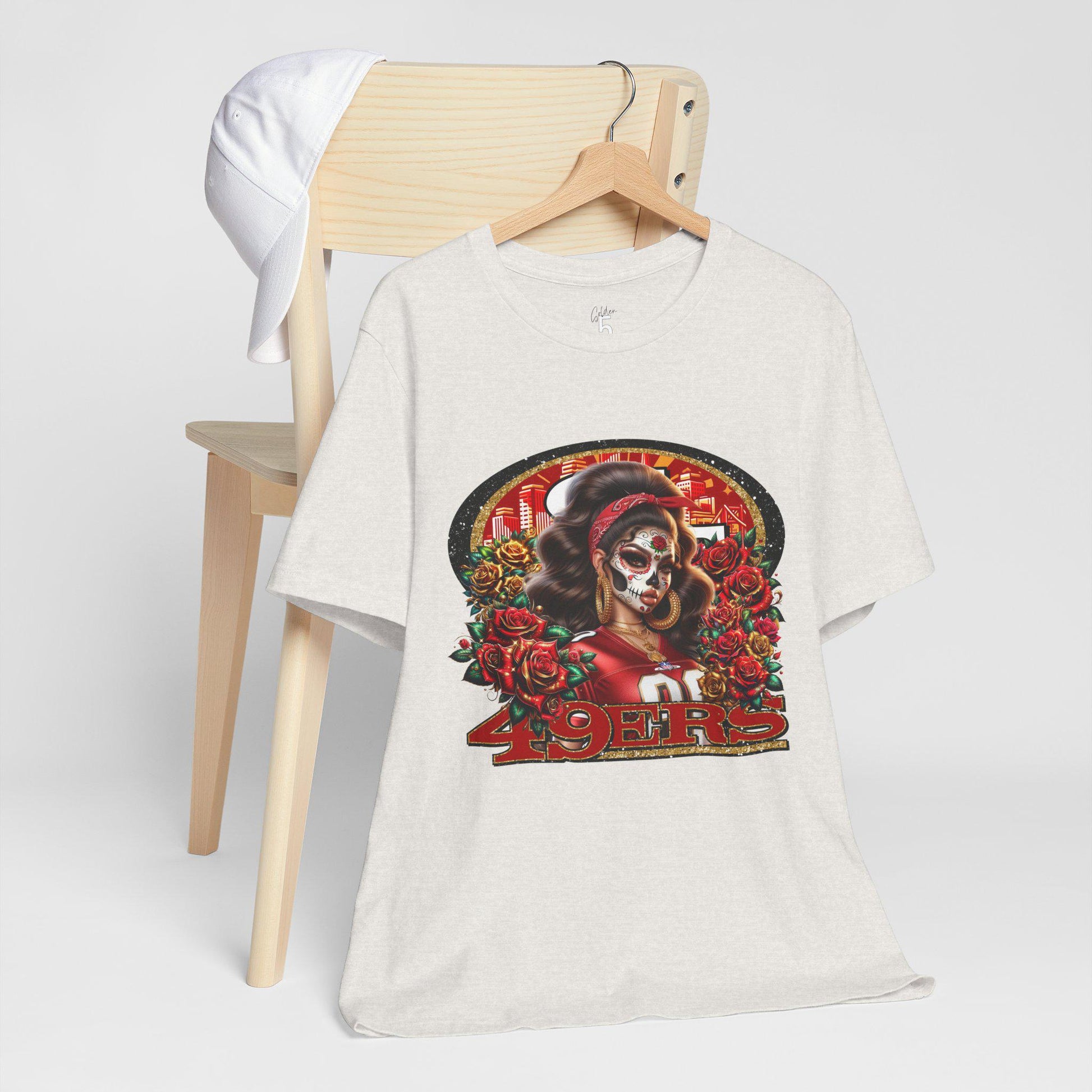 White t-shirt with a dia de los muertos niners design on a wooden chair against a white background