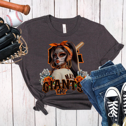 Dark gray t-shirt with a sf giants dia de los muertos design of a woman in a mask and hat, surrounded by roses, on a wooden surface with a baseball, bat, glove, jeans, and black sneakers.