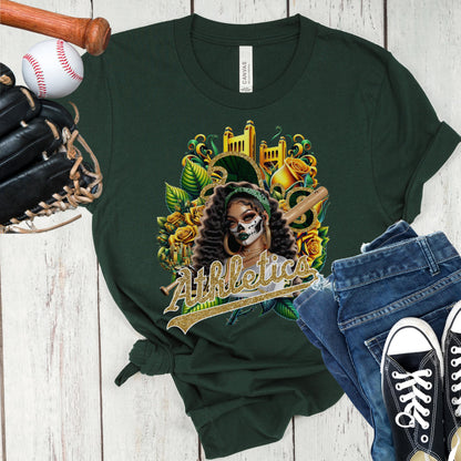 Green t-shirt with a dia de los muertos athletics design, displayed with a baseball bat, glove, jeans, and sneakers on a wooden surface.
