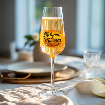 Glass of champagne with 'Melanin & Mimosas' text on a table setting.