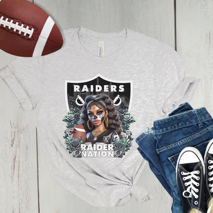 Gray t-shirt with a dia de los muertos Raiders design, football, jeans, and sneakers on a wooden surface