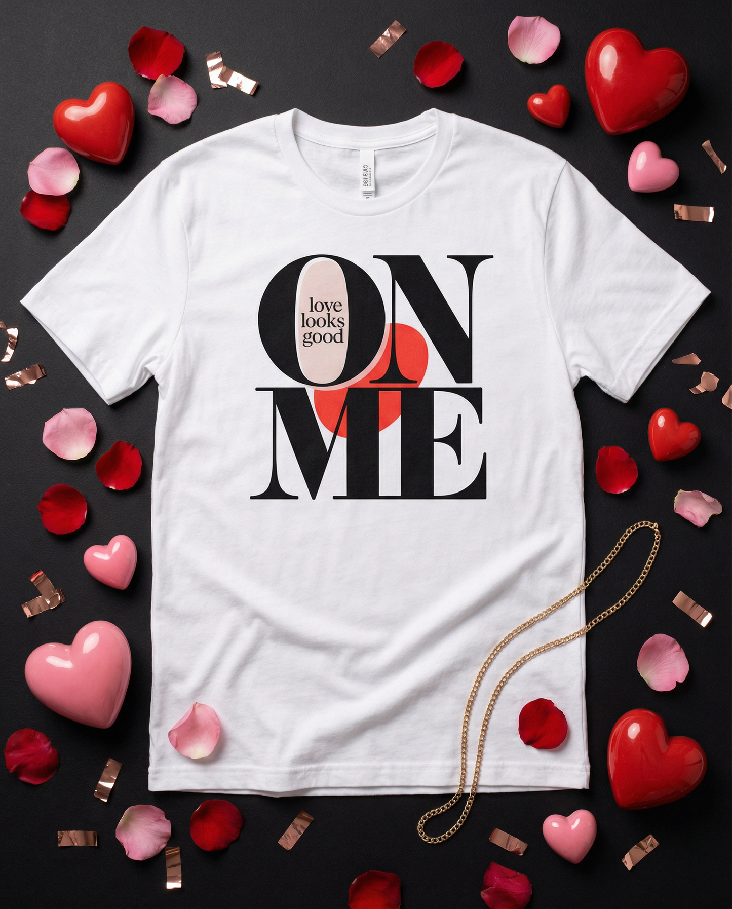 White t-shirt with 'Love looks good on me' design surrounded by heart-shaped objects on a dark background