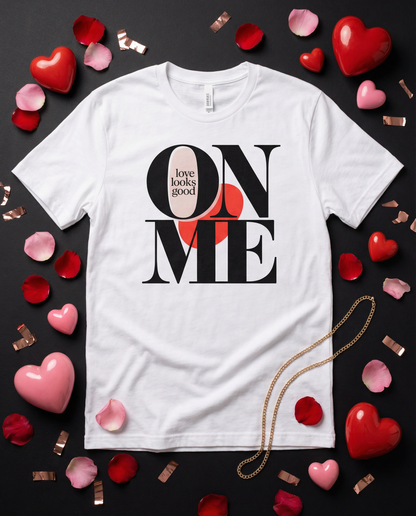 White t-shirt with 'Love looks good on me' design surrounded by heart-shaped objects on a dark background