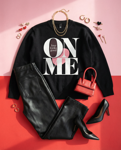 Black sweatshirt with 'Love looks good on me' text, black leather pants, red handbag, and black high heels on a pink and red gradient background.