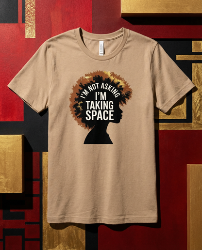 Beige t-shirt with a graphic of an afro and text 'I'm not asking, I'm taking space' on a geometric patterned background.