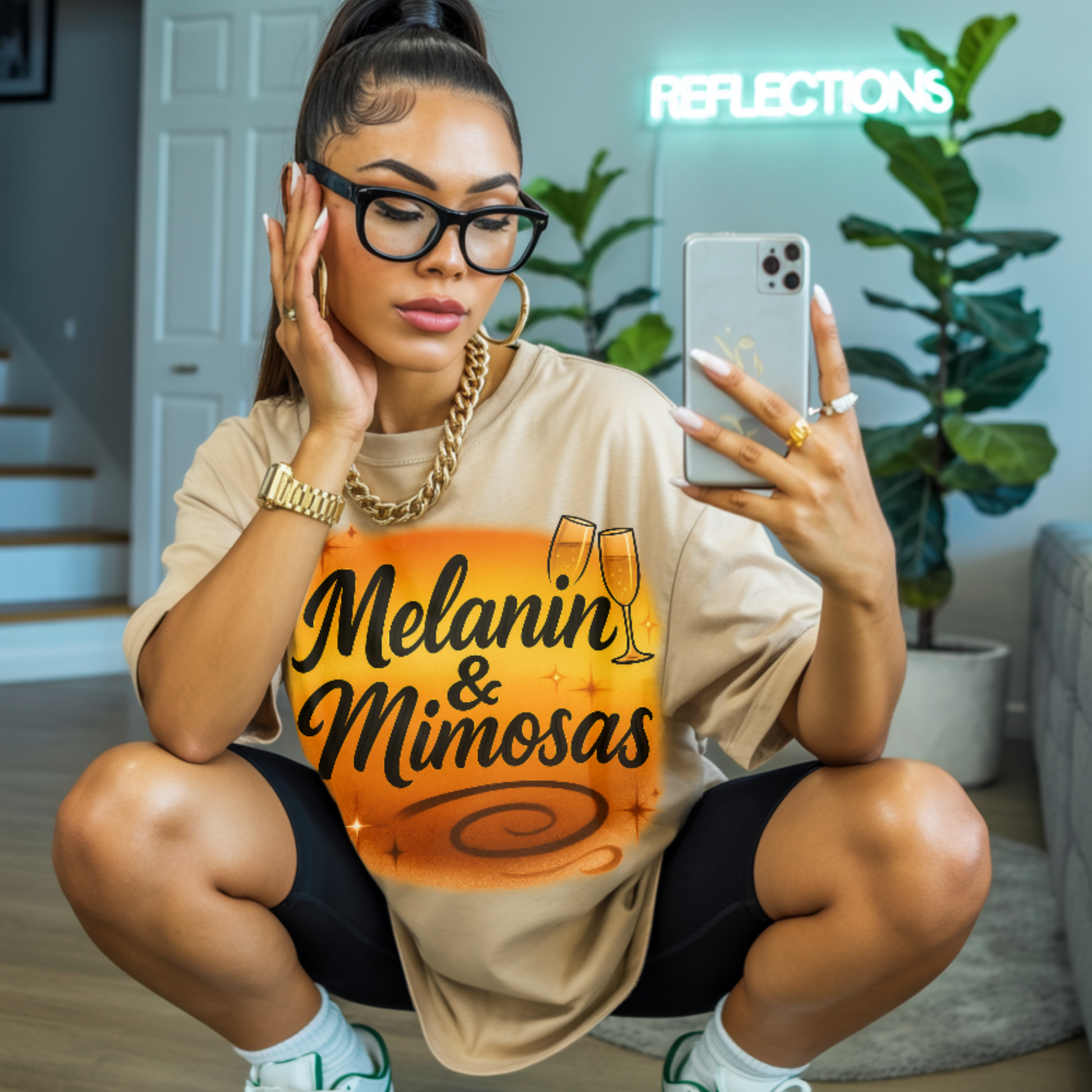Woman wearing a 'Melanin & Mimosas' shirt, sitting on the floor indoors.