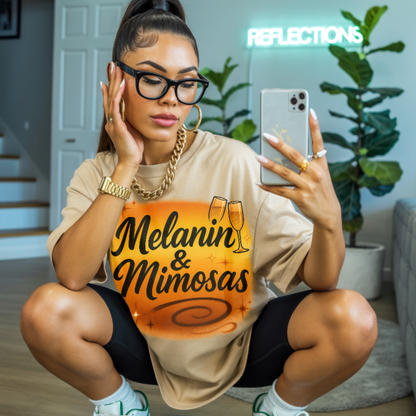 Woman wearing a 'Melanin & Mimosas' shirt, sitting on the floor indoors.