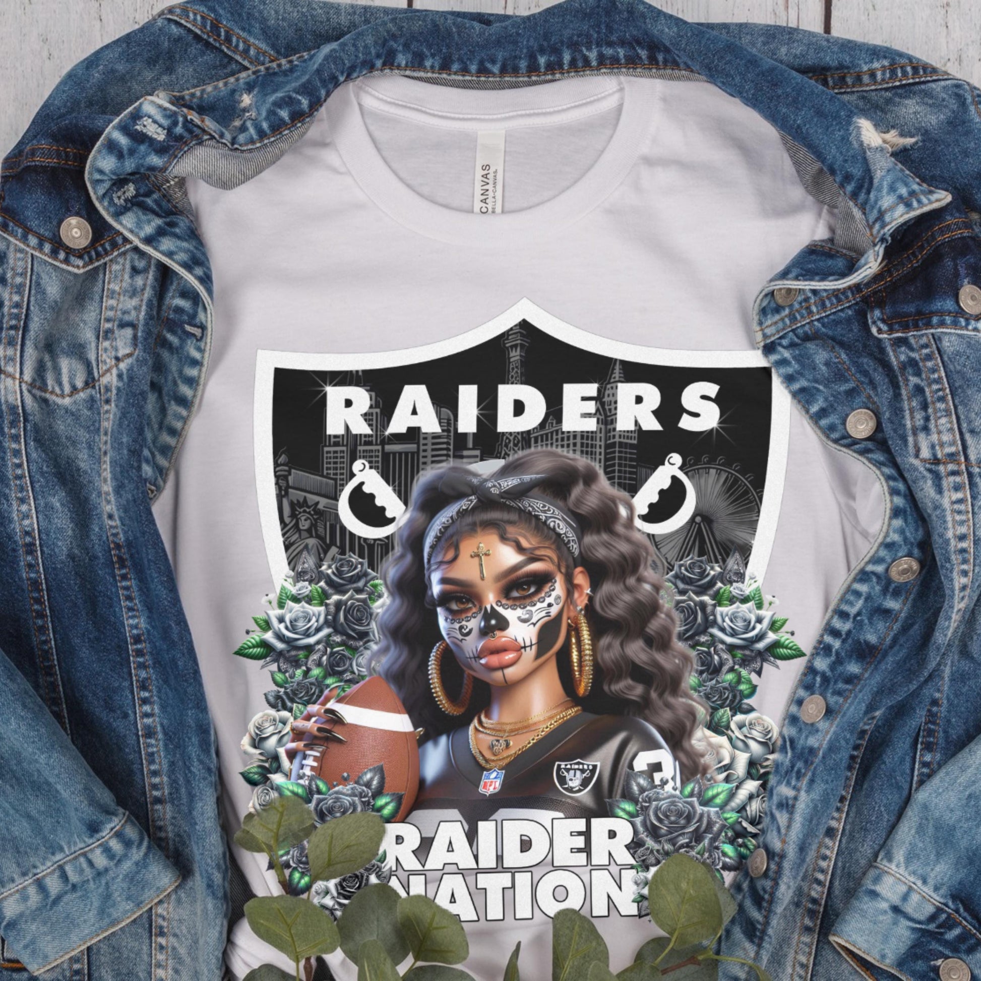 White t-shirt with a dia de los muertos Raiders design, displayed inside a denim jacket.