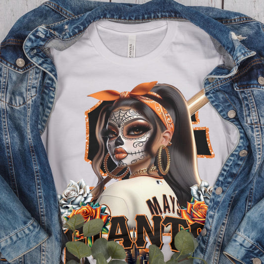 White t-shirt with a sf giants dia de los muertos design of a woman with a skull makeup, bandana, and baseball bat, worn with a denim jacket.