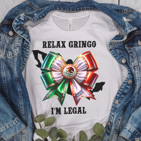 White t-shirt with Mexico bow graphic and text 'Relax Gringo I'm Legal' on a denim jacket background.