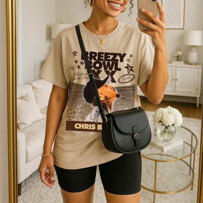 Person wearing a graphic t-shirt with with Breezy Bowl graphic, holding a phone, standing in a room.